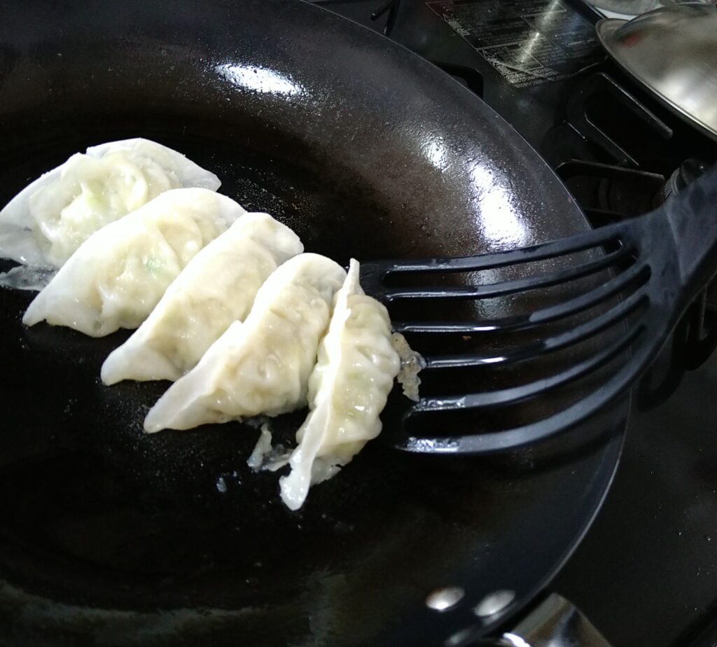 Silicone turner bending while trying to slide under gyoza in a pan
